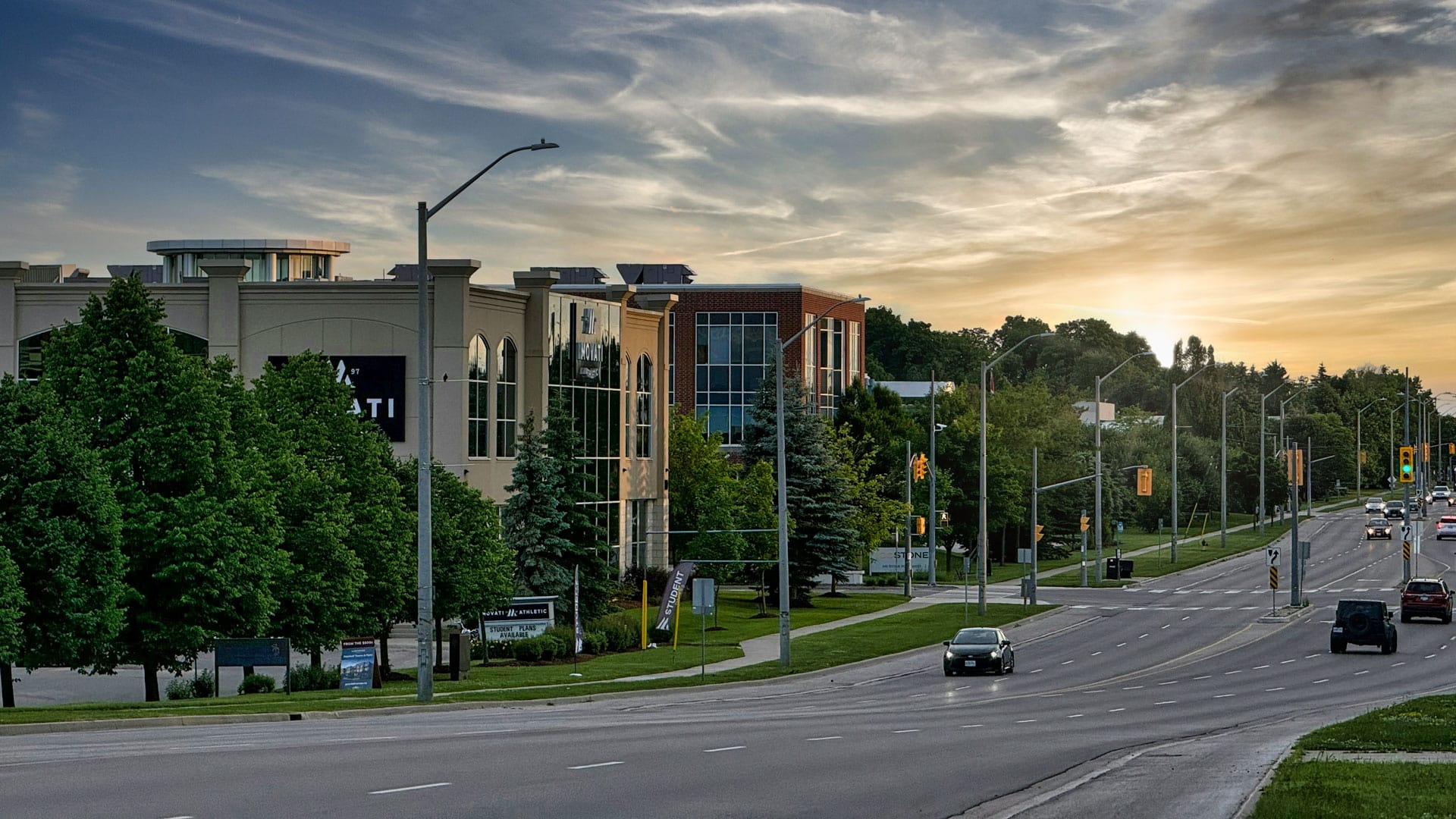 Modern commercial buildings with greenery along busy city street during sunset in Guelph, Ontario
